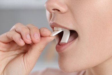 Woman putting chewing gum into mouth on blurred background, closeup