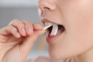 Photo of Woman putting chewing gum into mouth on blurred background, closeup