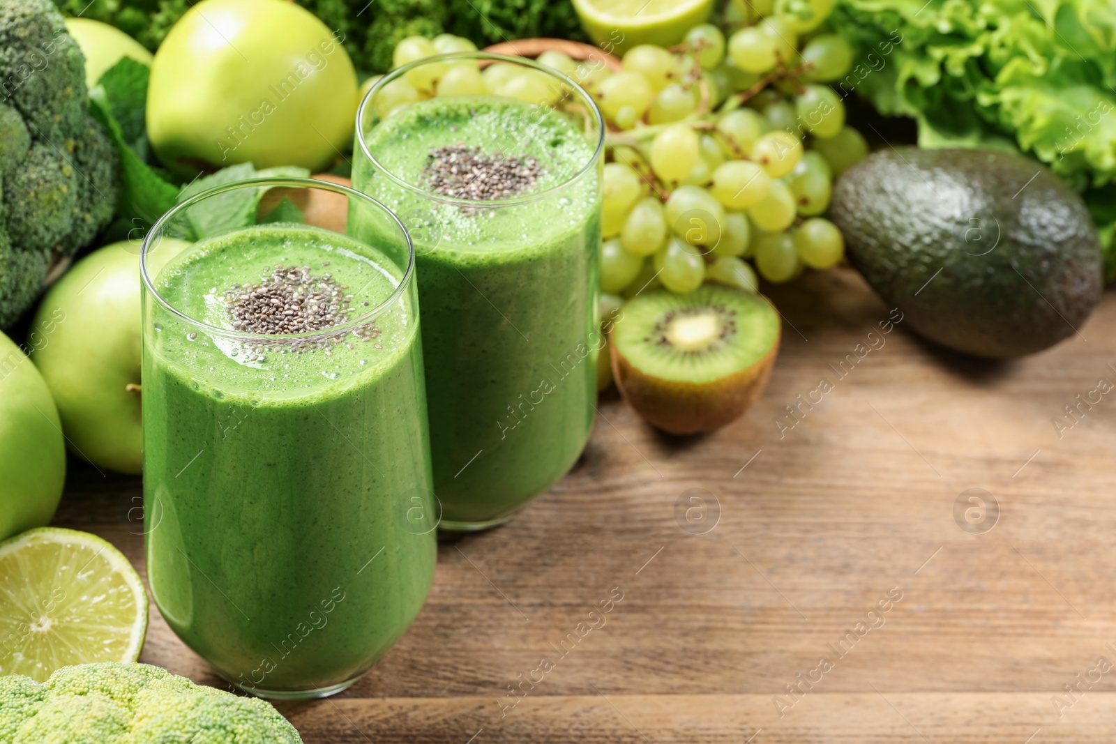 Photo of Glasses of fresh green smoothie and ingredients on wooden table, space for text