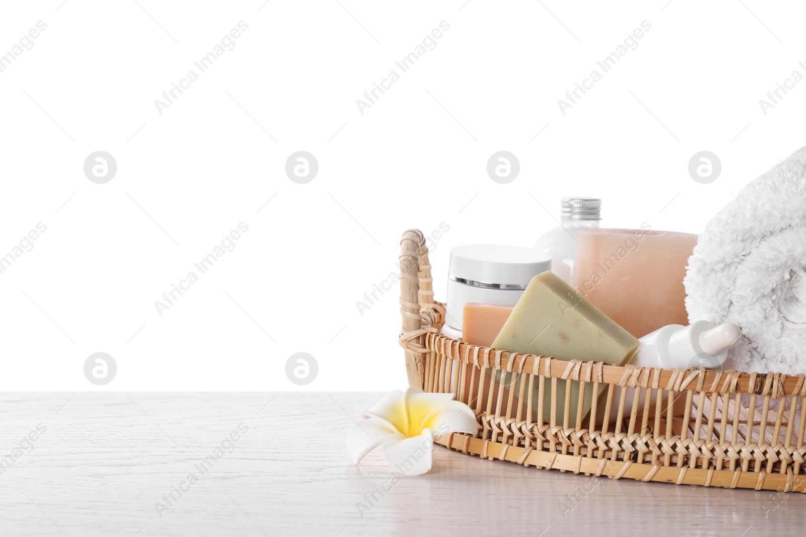 Photo of Wicker tray with towel, plumeria flower and toiletries on white wooden table. Spa treatment