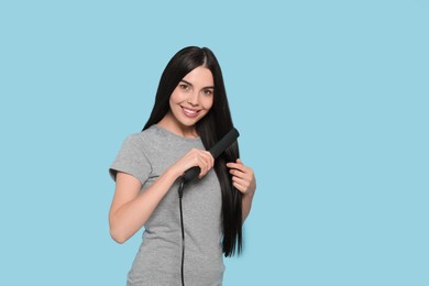 Beautiful happy woman using hair iron on light blue background. Space for text