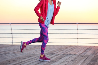 Photo of Young woman listening to music and running on pier in morning