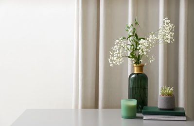Photo of Vase with beautiful flowers, candle and books on grey table indoors, space for text. Interior elements