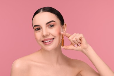 Photo of Beautiful young woman holding skincare ampoule on pink background