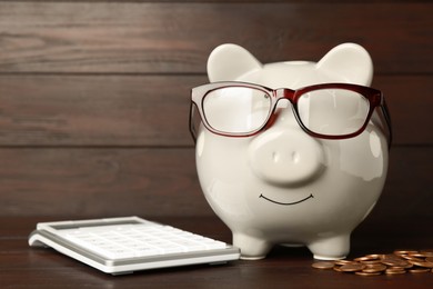 Photo of Piggy bank with glasses, calculator and coins on wooden table