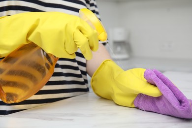 Woman cleaning white surface with detergent and purple rag indoors, closeup
