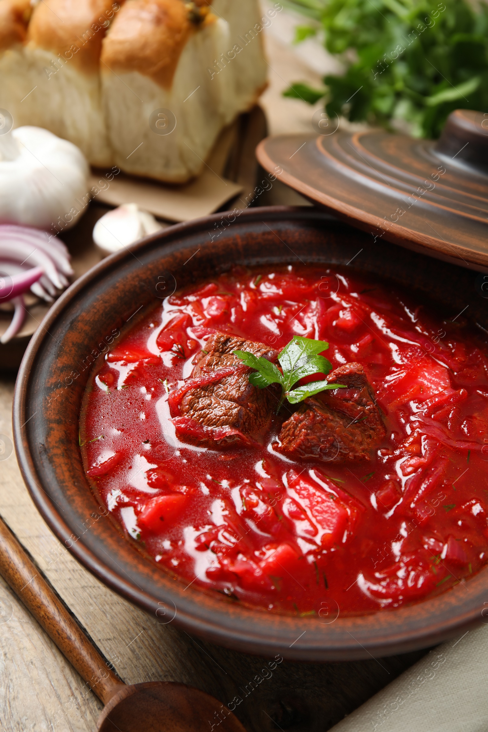 Photo of Stylish brown clay bowl with Ukrainian borsch served on wooden table