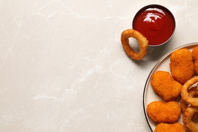 Tasty fried onion rings, chicken nuggets and ketchup on light grey marble table, flat lay. Space for text