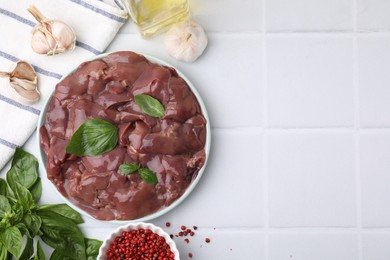 Photo of Plate of raw chicken liver with basil and products on white tiled table, flat lay. Space for text
