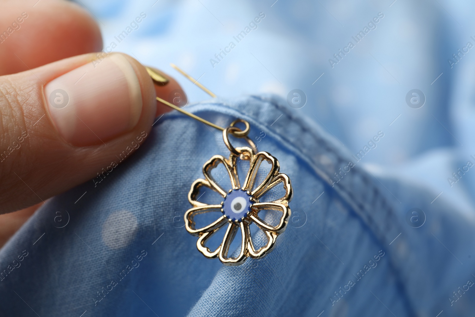 Photo of Woman pinning evil eye amulet on clothing, closeup