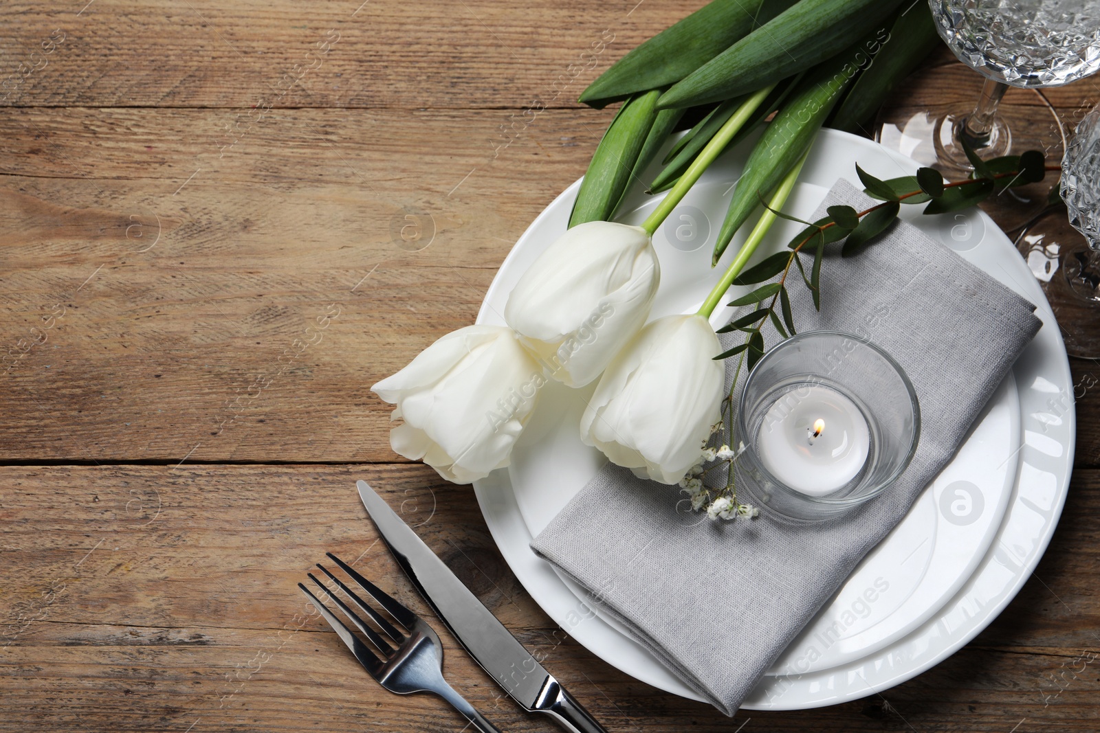 Photo of Stylish table setting with cutlery, burning candle and tulips on wooden background, flat lay. Space for text