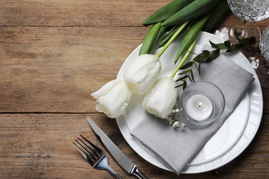 Photo of Stylish table setting with cutlery, burning candle and tulips on wooden background, flat lay. Space for text