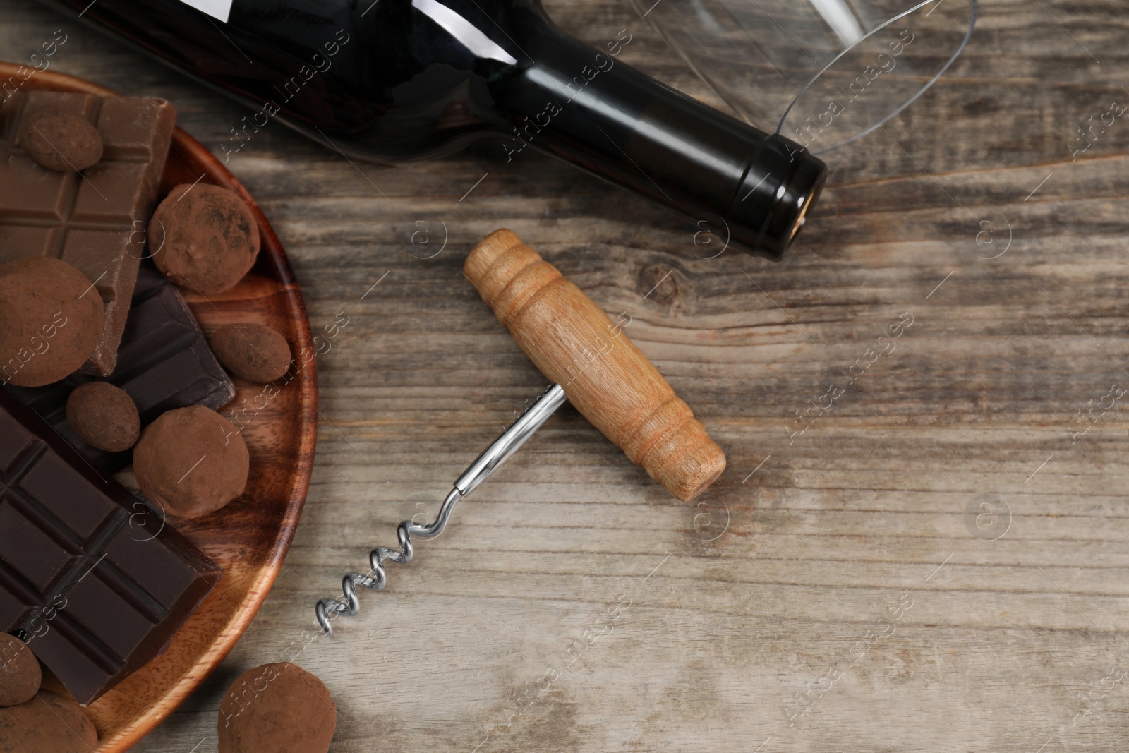 Photo of Bottle of red wine, glass, chocolate sweets and corkscrew on wooden table, above view. Space for text
