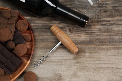 Bottle of red wine, glass, chocolate sweets and corkscrew on wooden table, above view. Space for text