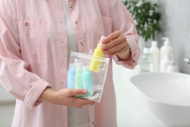 Photo of Woman packing cosmetic travel kit in bathroom, closeup. Bath accessories