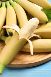 Photo of Tasty ripe baby bananas on light blue wooden table, closeup