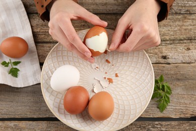 Photo of Woman peeling boiled egg at old wooden table, top view