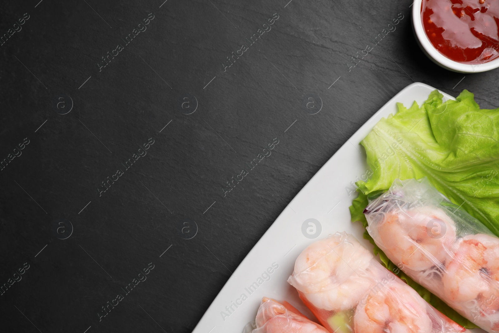 Photo of Delicious spring rolls with shrimps wrapped in rice paper served on black table, flat lay. Space for text