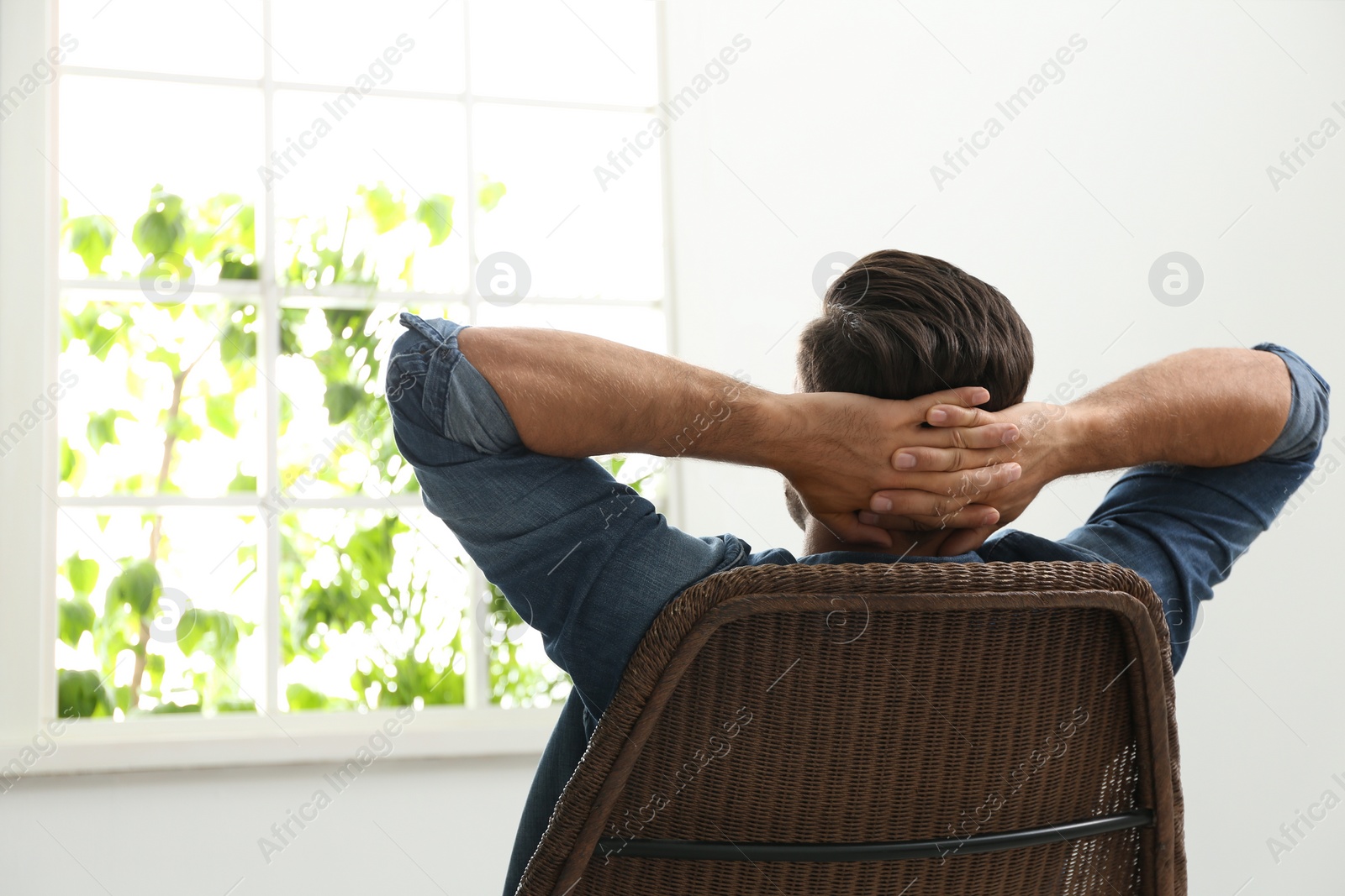 Photo of Man relaxing in armchair near window at home, back view