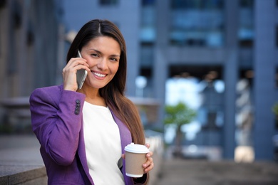 Photo of Beautiful businesswoman with cup of coffee talking on phone outdoors. Space for text