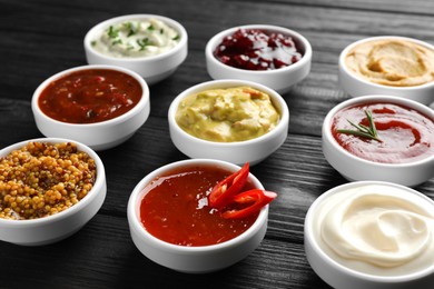 Different tasty sauces in bowls on black wooden table, closeup