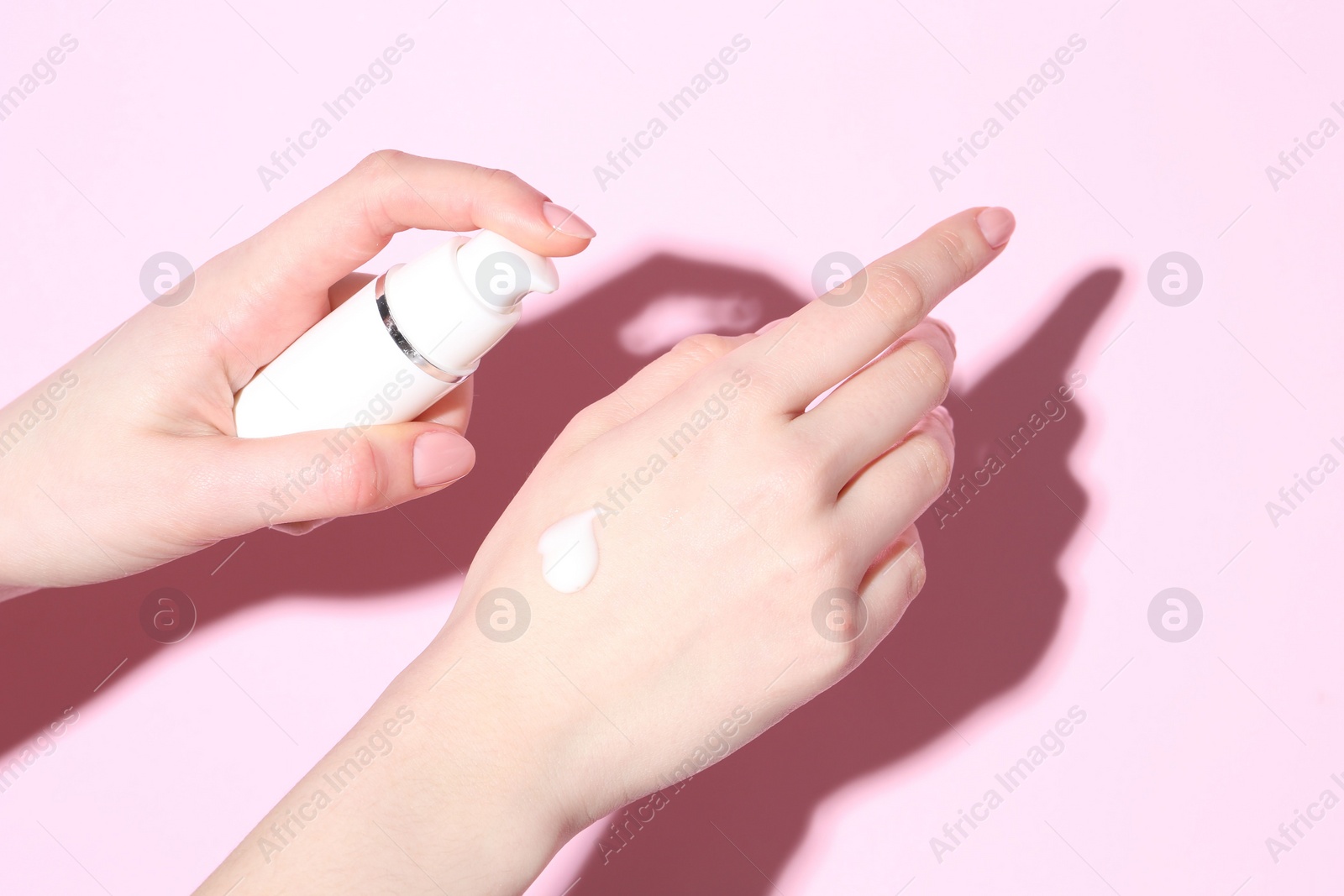 Photo of Woman applying cream on her hand against pink background, closeup