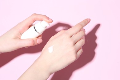 Woman applying cream on her hand against pink background, closeup