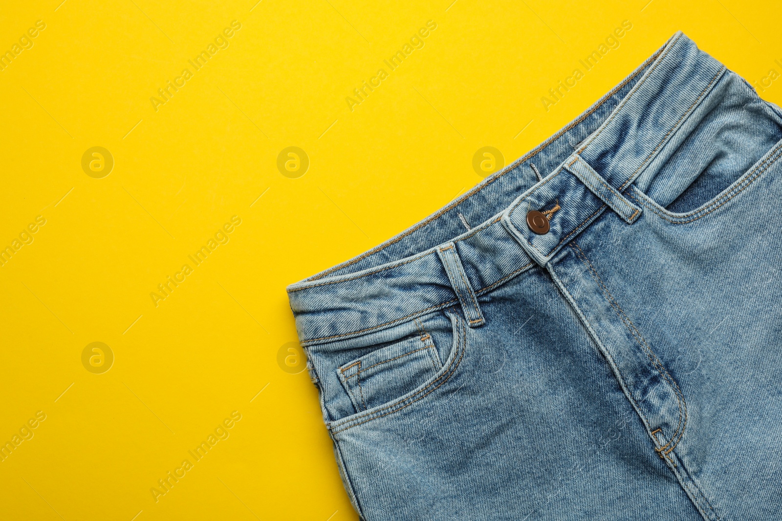 Photo of Stylish jeans on yellow background, top view