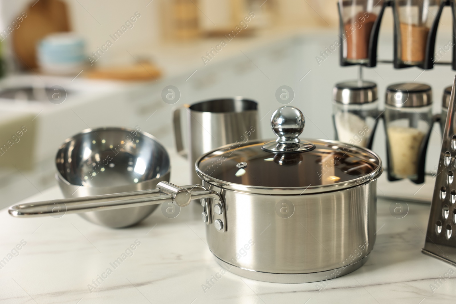 Photo of Set of shiny cooking utensils and spices on white table against blurred background