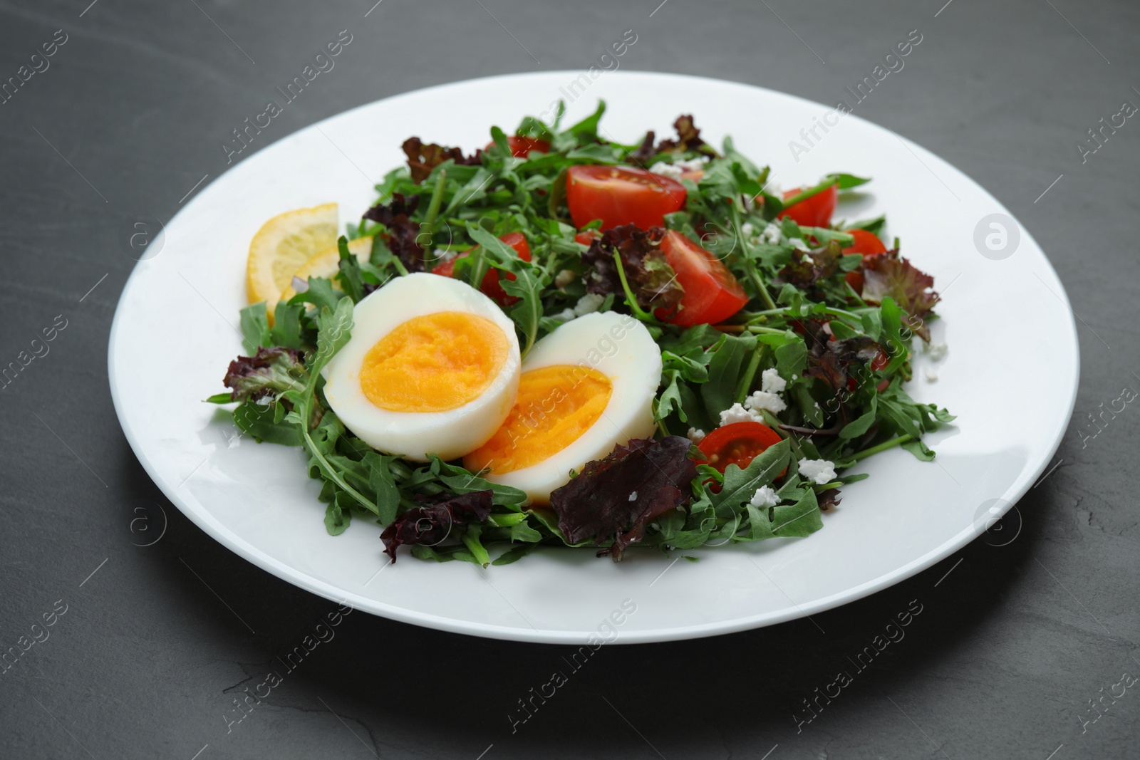 Photo of Delicious salad with boiled egg, arugula and tomatoes on black table, closeup