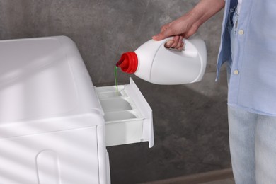 Woman pouring fabric softener from bottle into washing machine indoors, closeup