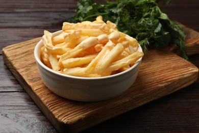 Photo of Delicious french fries with cheese sauce in bowl on wooden table