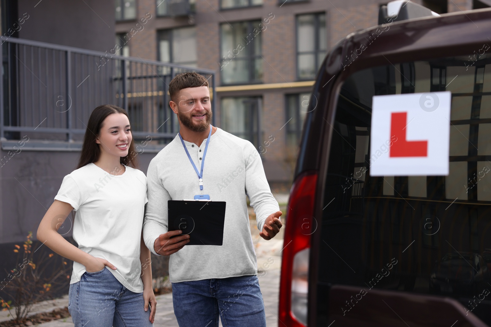 Photo of Learner driver and instructor near car with L-plate outdoors. Driving school