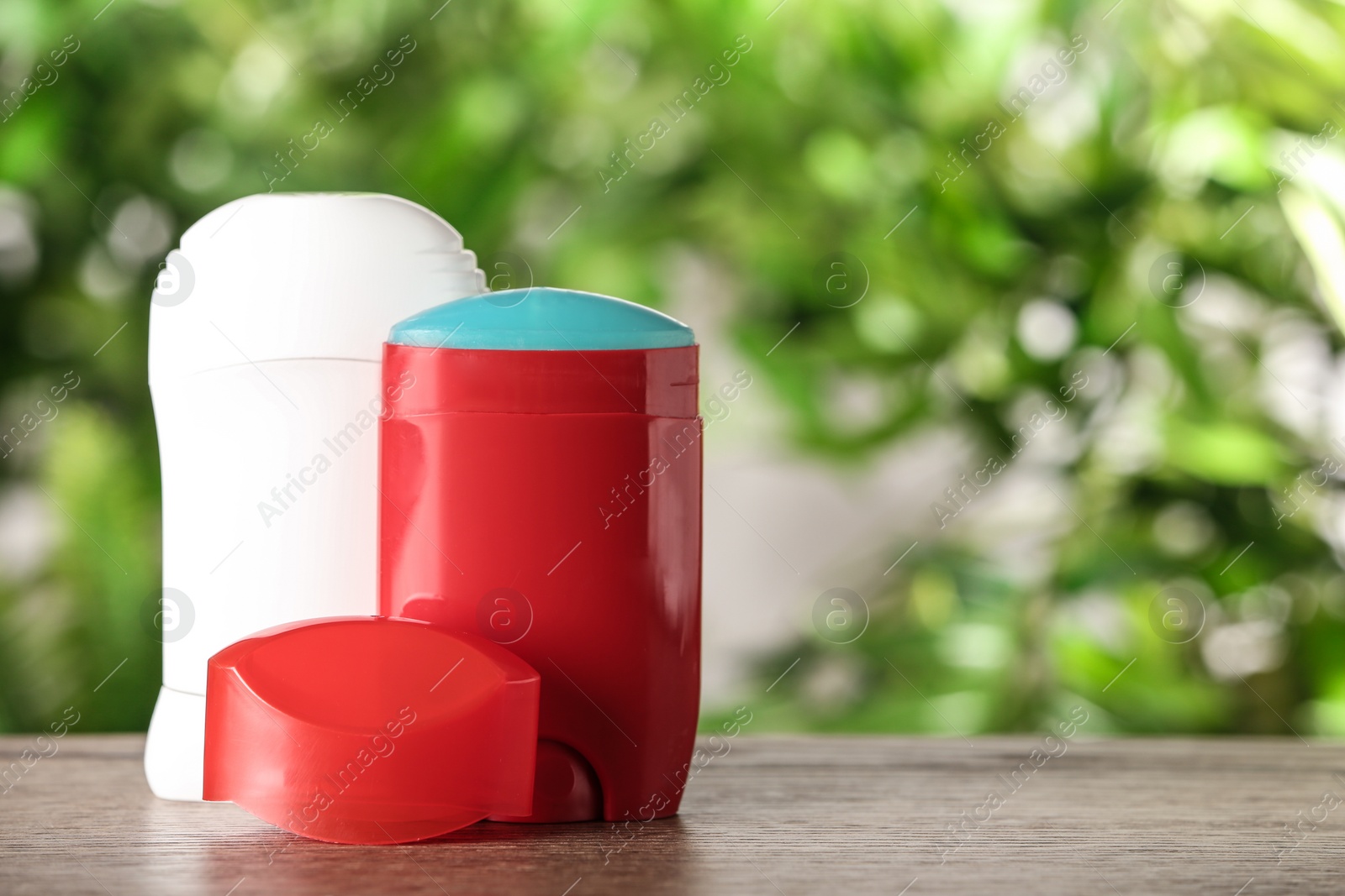 Photo of Different deodorants on wooden table against blurred background. Space for text