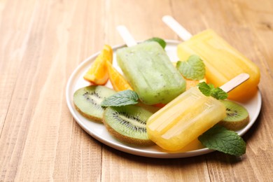 Photo of Plate of tasty orange and kiwi ice pops on wooden table. Fruit popsicle