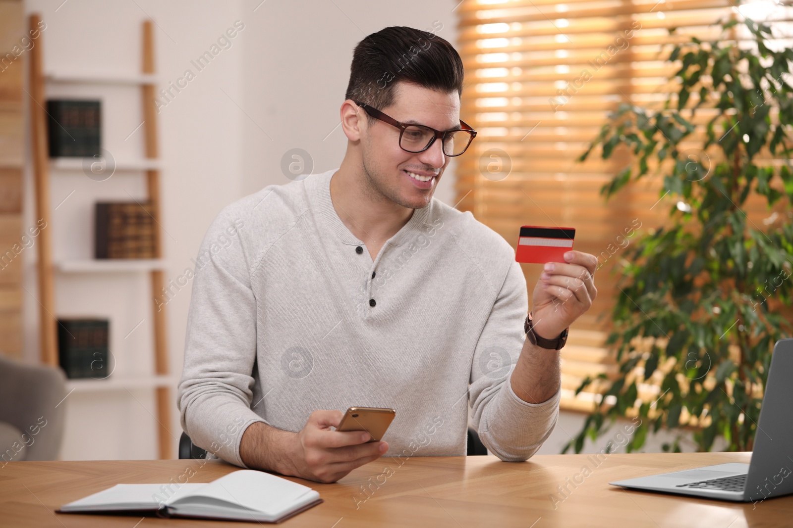 Photo of Man using smartphone and credit card for online payment at desk in room