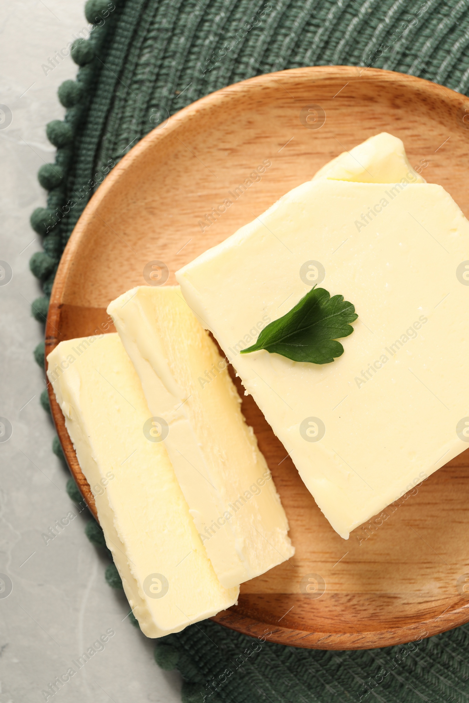 Photo of Cut tasty butter with parsley on grey table, top view