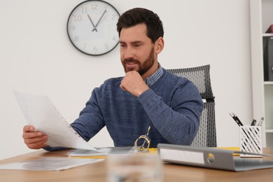 Photo of Businessman reading document at wooden table in office