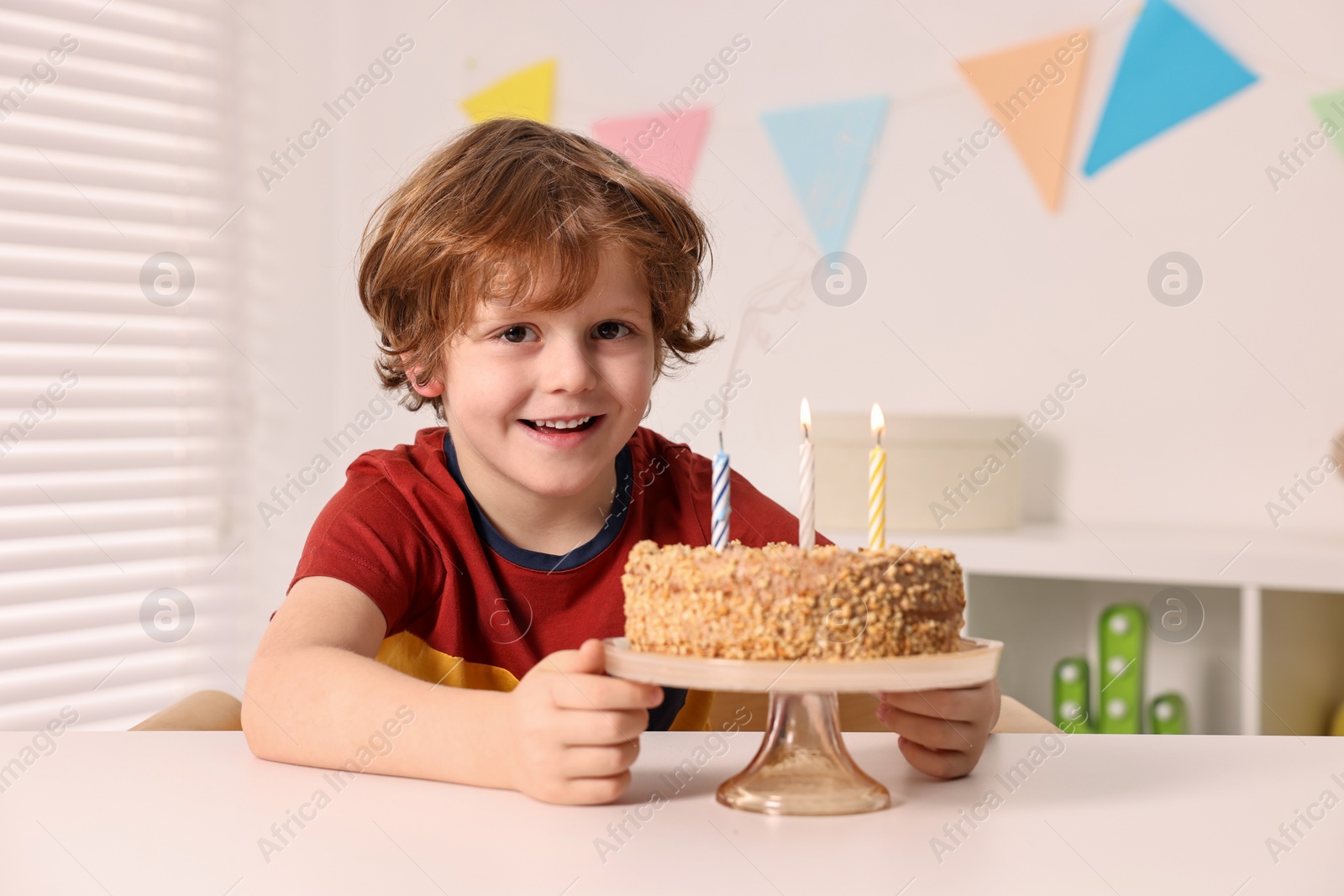 Photo of Cute boy with birthday cake at table indoors