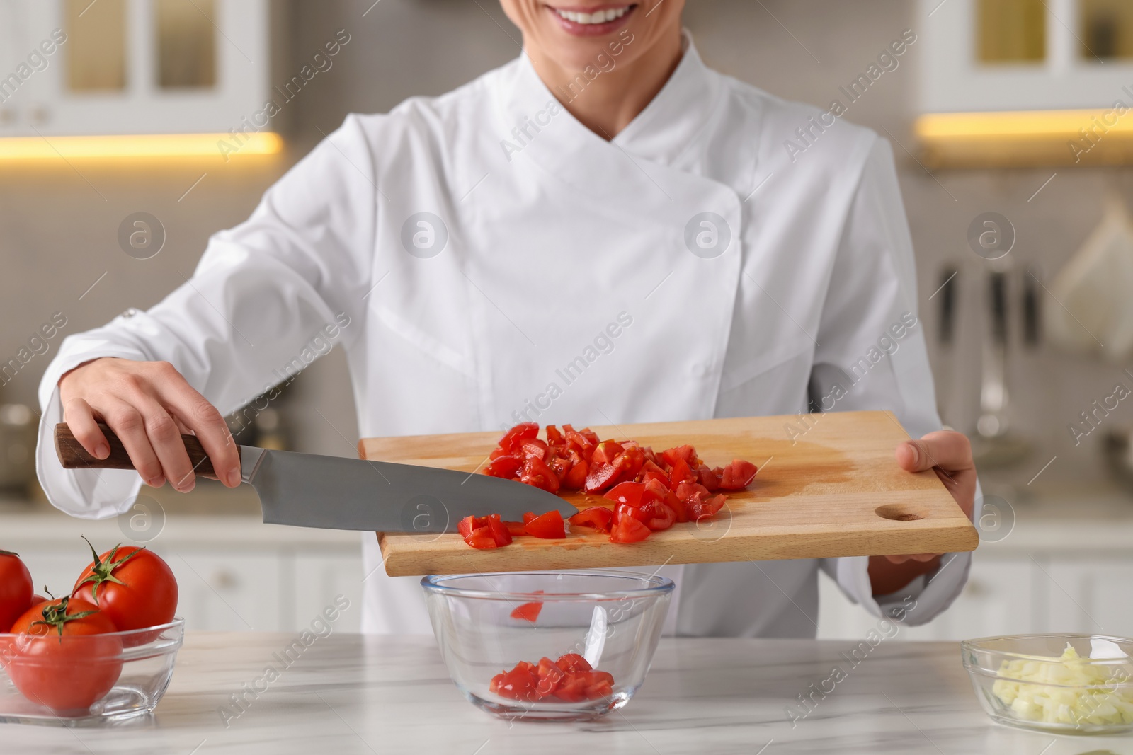 Photo of Professional chef putting cut tomatoes into bowl at white marble table indoors, closeup