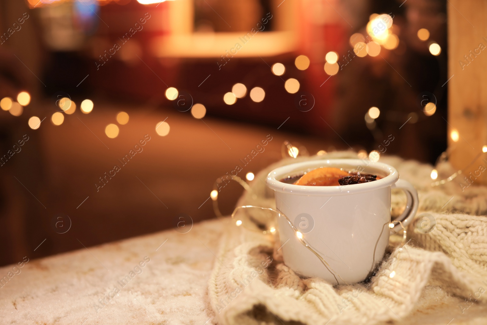 Photo of Cup of hot mulled wine and garland on table against blurred background. Space for text