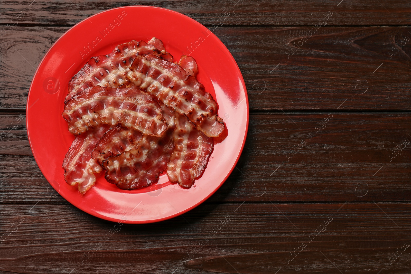 Photo of Plate with fried bacon slices on wooden table, top view. Space for text