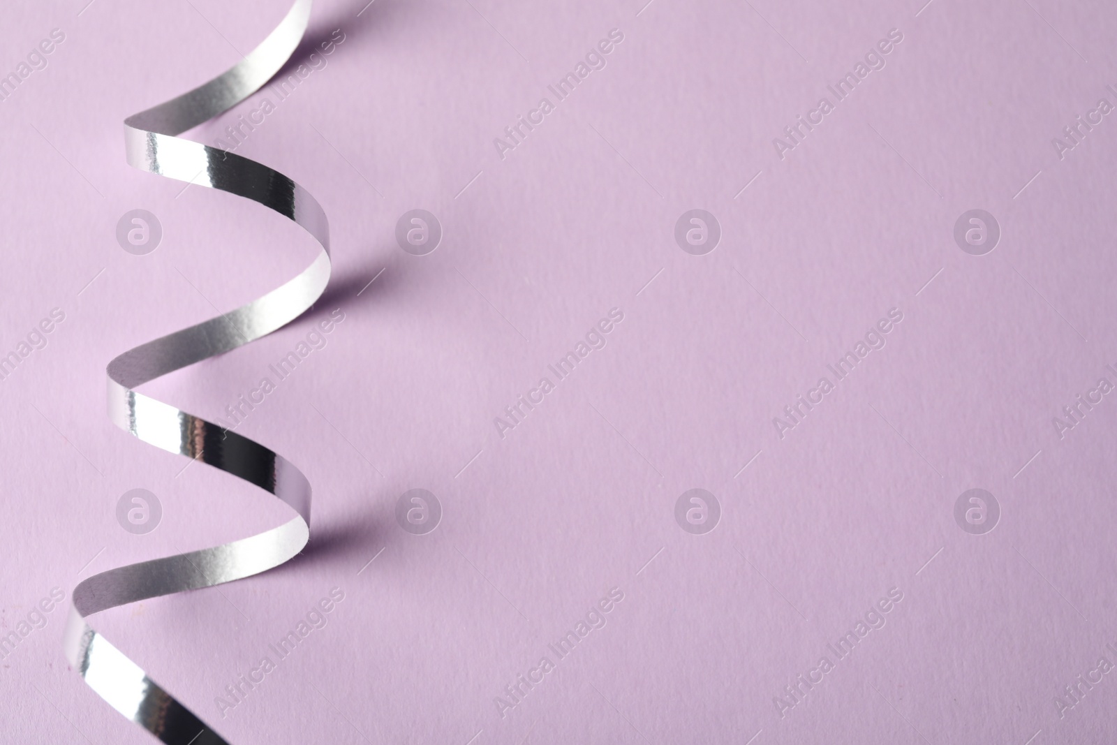 Photo of Shiny serpentine streamer on lilac background, top view. Space for text