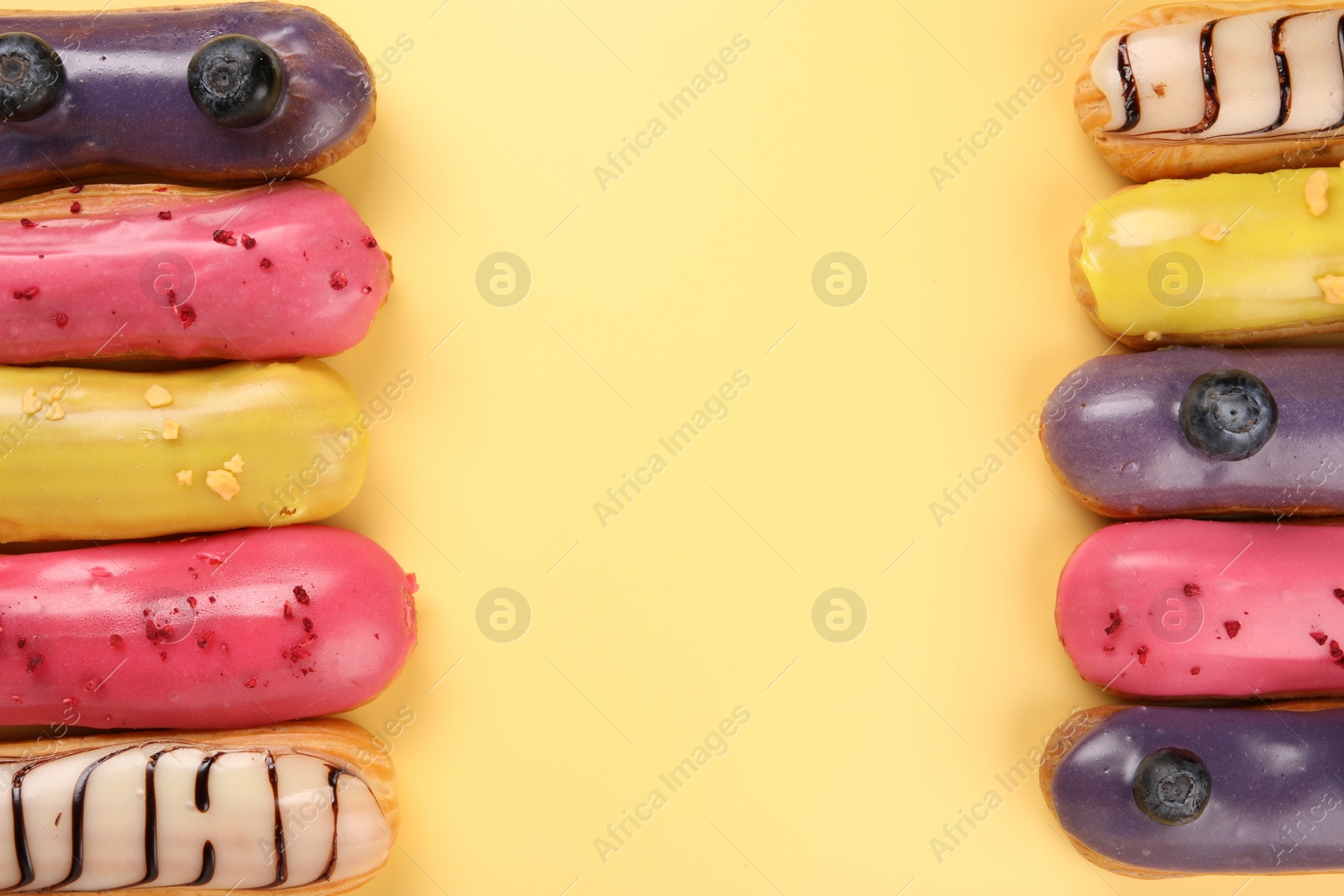 Photo of Delicious eclairs covered with glaze on yellow background, flat lay. Space for text