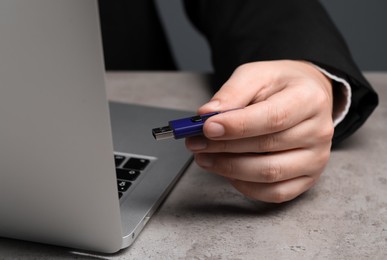 Photo of Man with usb flash drive near laptop at grey table, closeup