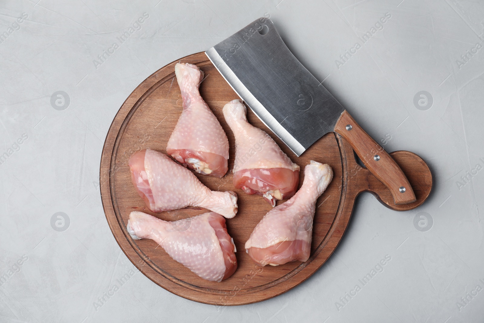 Photo of Wooden board with raw chicken drumsticks and butcher knife on gray background, top view. Fresh meat