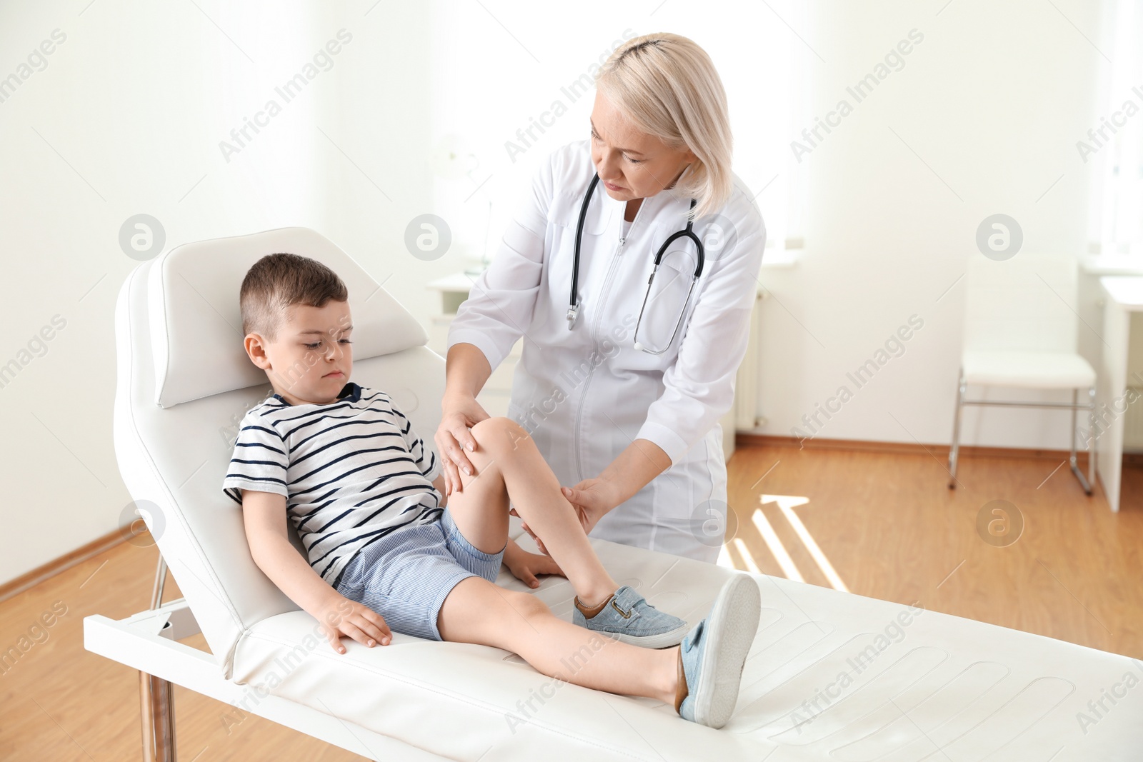 Photo of Doctor examining little patient with knee problem in clinic