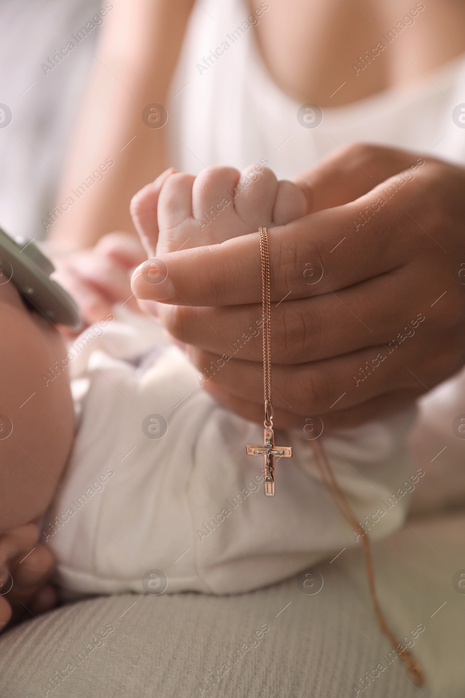 Photo of Mother holding Christian cross near newborn baby indoors, closeup