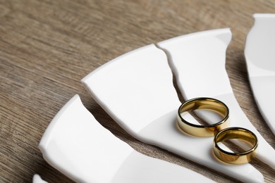 Photo of Divorce concept. Broken plate and rings on wooden table, closeup