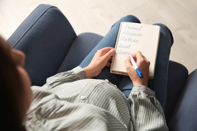 Pregnant woman with baby names list sitting in armchair, closeup